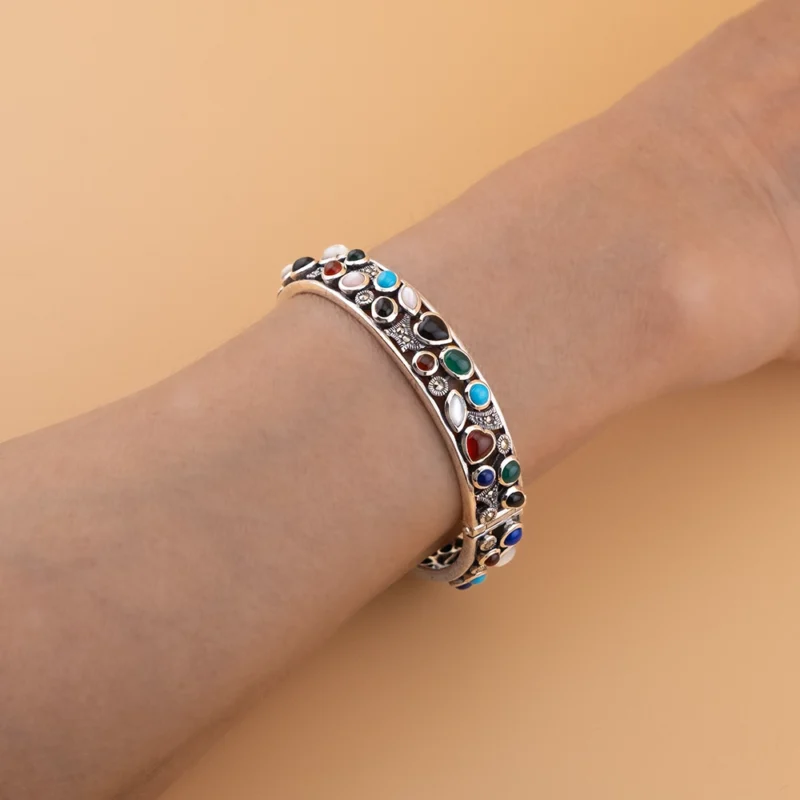 أسوارة فضة عيار 925 على المعصم بأحجار طبيعية متعددة الألوان تبرز تفاصيل التصميم العتيق.